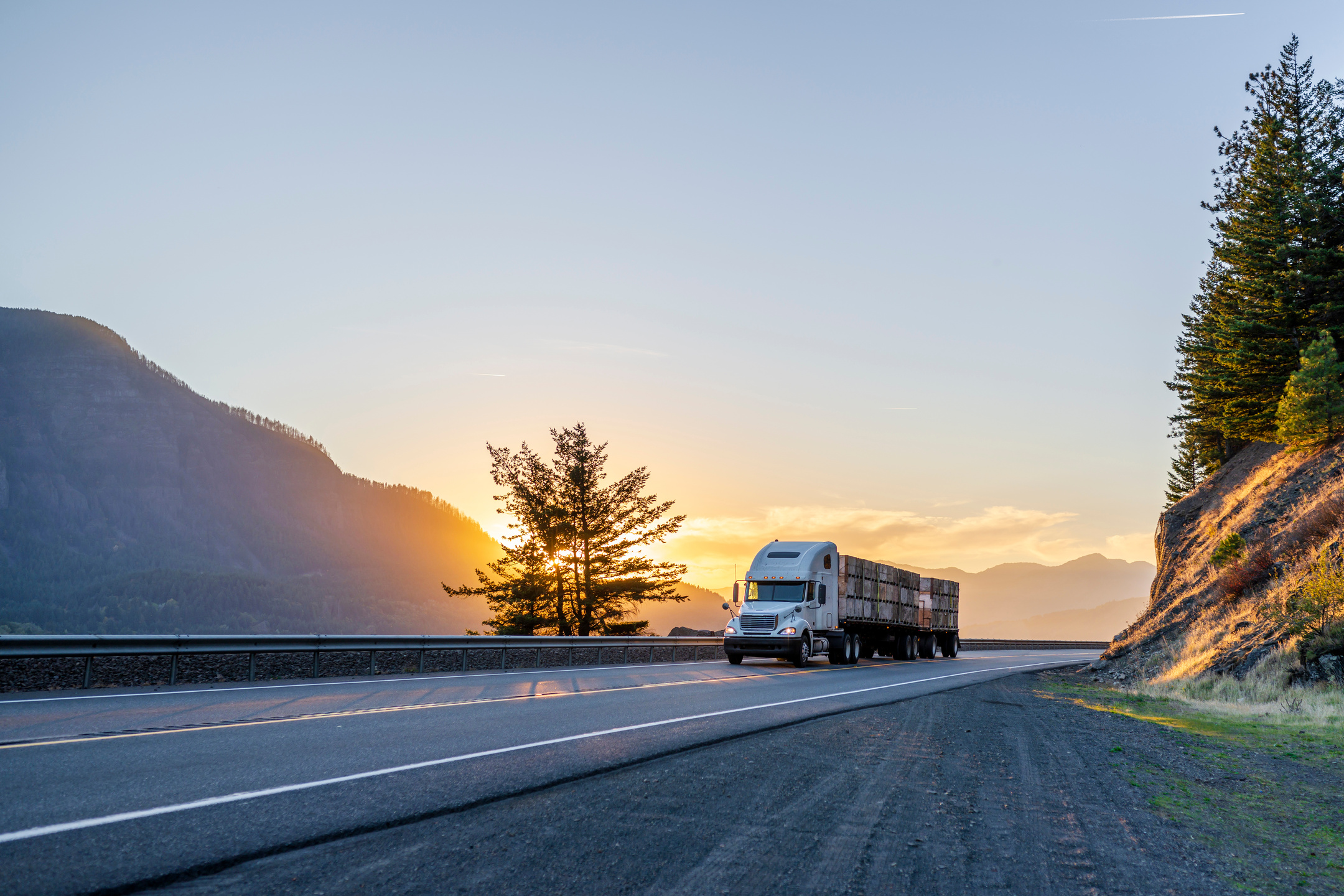 Big rig semi truck transporting boxes with apples on flat bed semi trailer on evening road